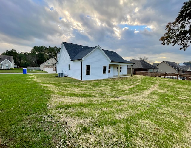 rear view of house with central air condition unit and a lawn