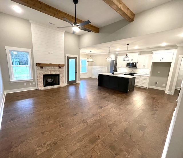 kitchen with ceiling fan, hanging light fixtures, beamed ceiling, an island with sink, and white cabinets