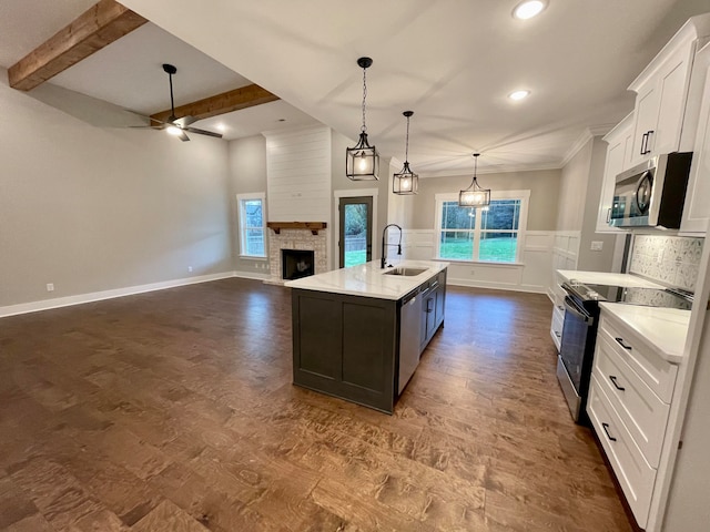 kitchen with appliances with stainless steel finishes, a kitchen island with sink, pendant lighting, beam ceiling, and white cabinets