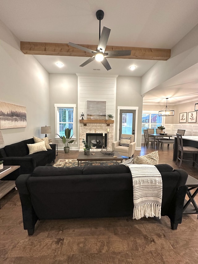 living room with beam ceiling, ceiling fan with notable chandelier, dark hardwood / wood-style floors, and a stone fireplace