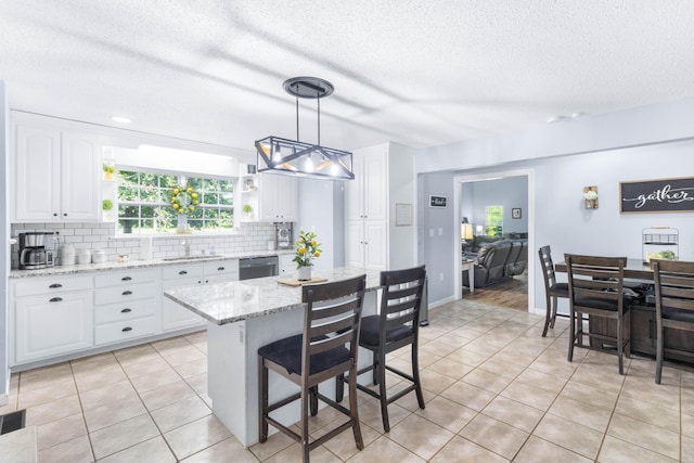 kitchen with white cabinetry, a center island, light stone counters, stainless steel dishwasher, and pendant lighting