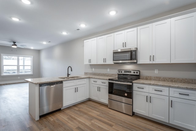 kitchen with white cabinets, sink, light hardwood / wood-style flooring, appliances with stainless steel finishes, and kitchen peninsula