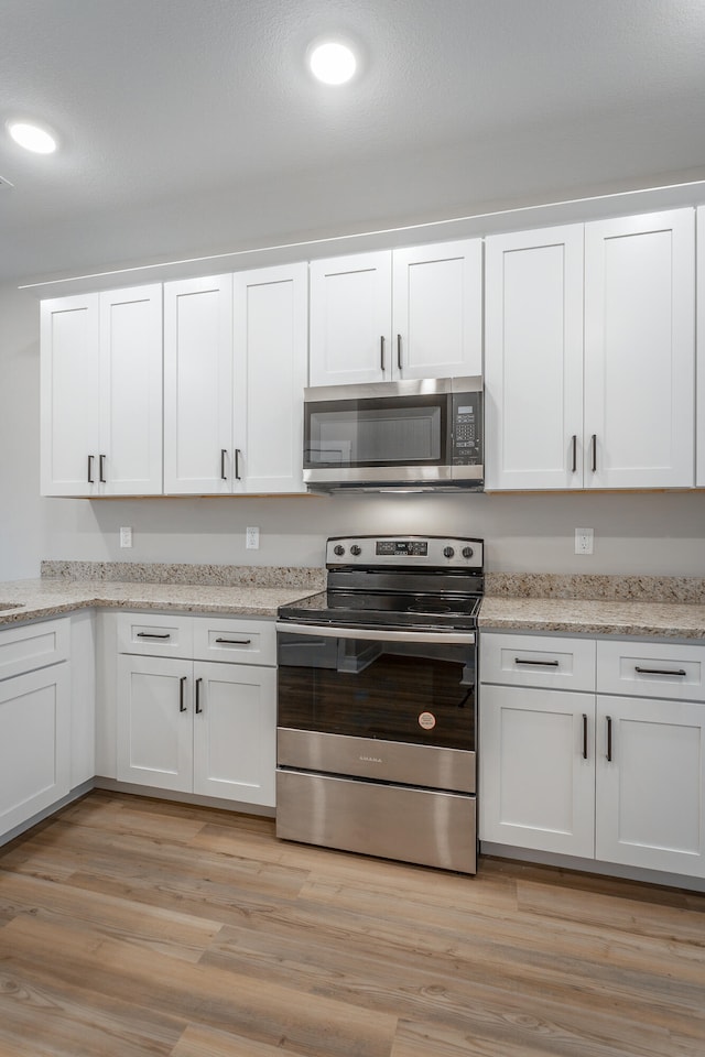 kitchen with white cabinets, light wood-type flooring, stainless steel appliances, and light stone countertops