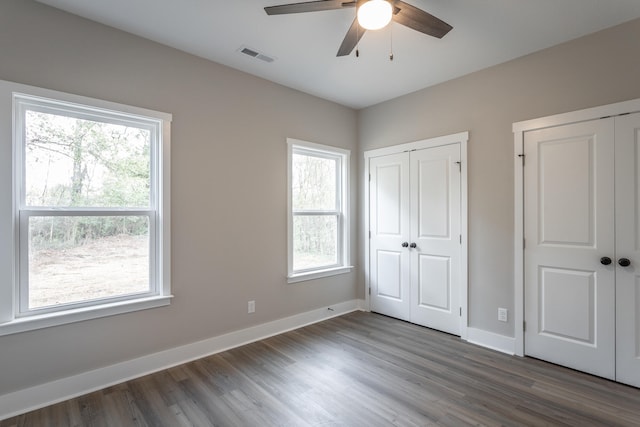 unfurnished bedroom with multiple windows, ceiling fan, two closets, and dark hardwood / wood-style floors