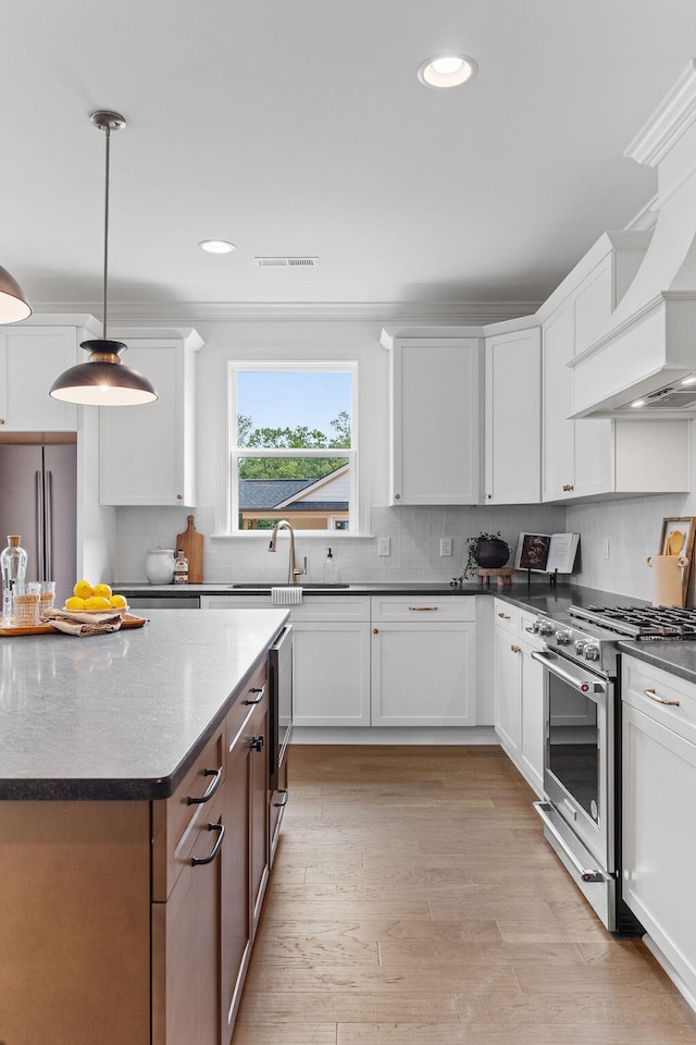 kitchen featuring white cabinets, premium appliances, light hardwood / wood-style floors, and hanging light fixtures