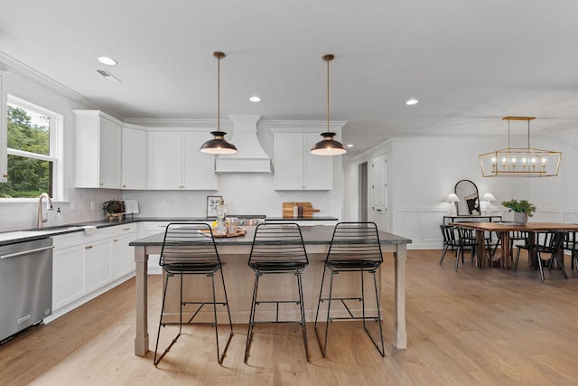 kitchen featuring stainless steel dishwasher, a kitchen island, white cabinets, and hanging light fixtures