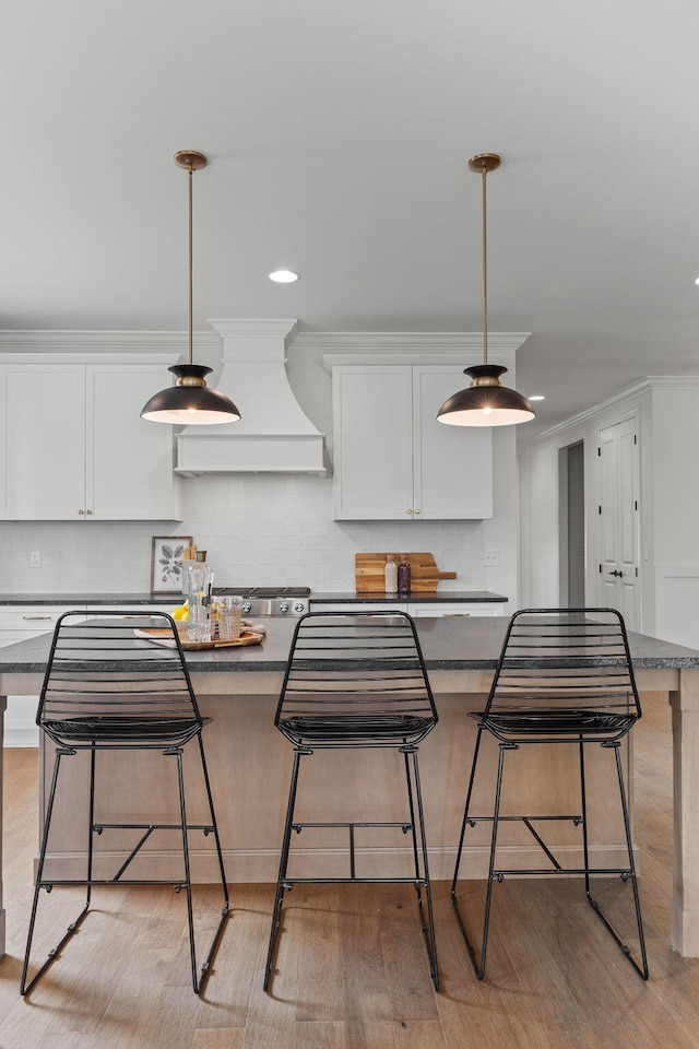 kitchen featuring a breakfast bar, light hardwood / wood-style flooring, white cabinets, and custom exhaust hood