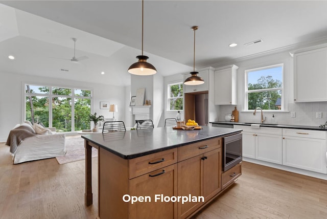 kitchen featuring a kitchen breakfast bar, white cabinets, light hardwood / wood-style floors, a kitchen island, and stainless steel microwave