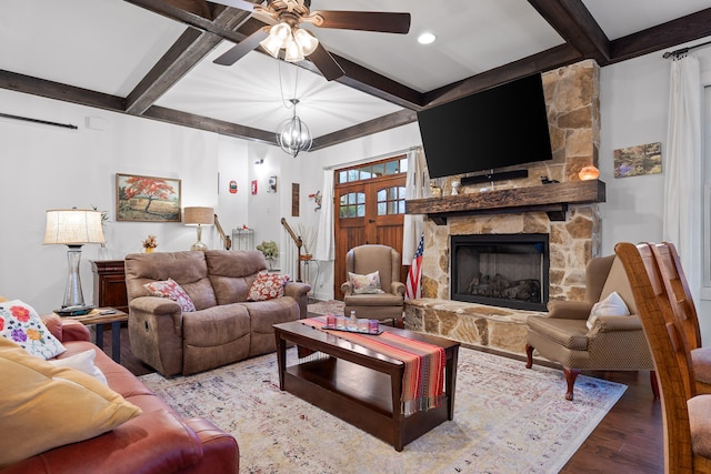 living room featuring beam ceiling, a stone fireplace, ceiling fan with notable chandelier, and hardwood / wood-style flooring