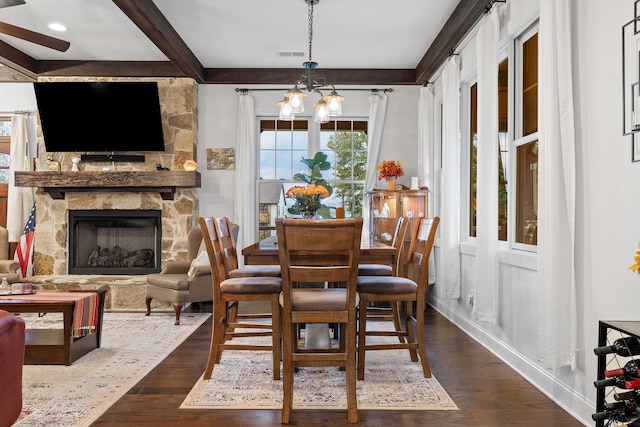 dining space with beamed ceiling, dark hardwood / wood-style floors, a stone fireplace, and a chandelier