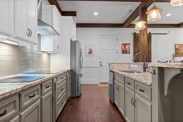 kitchen featuring dark wood-type flooring, wall chimney range hood, sink, decorative light fixtures, and light stone counters