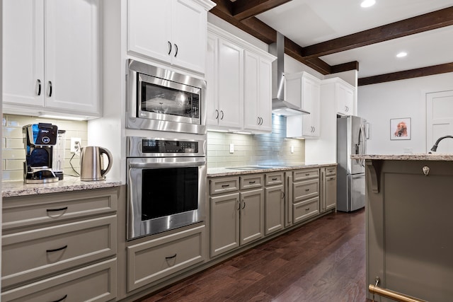 kitchen featuring appliances with stainless steel finishes, dark hardwood / wood-style flooring, white cabinets, wall chimney range hood, and beamed ceiling