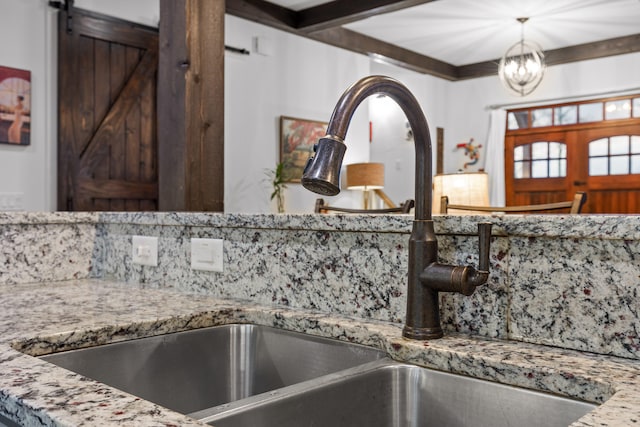 interior details with beam ceiling, a barn door, backsplash, and sink