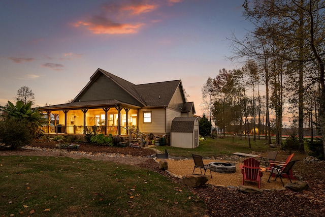 back house at dusk featuring covered porch, an outdoor fire pit, a storage shed, and a lawn