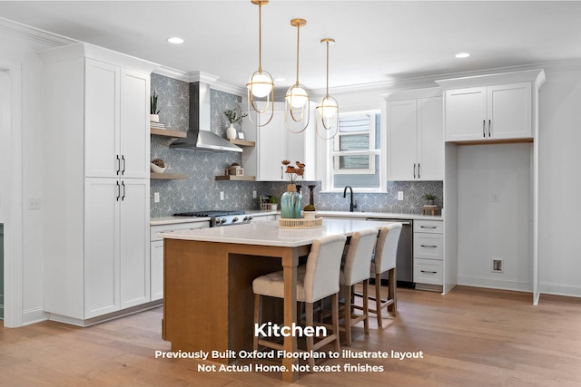 kitchen featuring white cabinetry, wall chimney exhaust hood, stainless steel appliances, light hardwood / wood-style floors, and a kitchen island