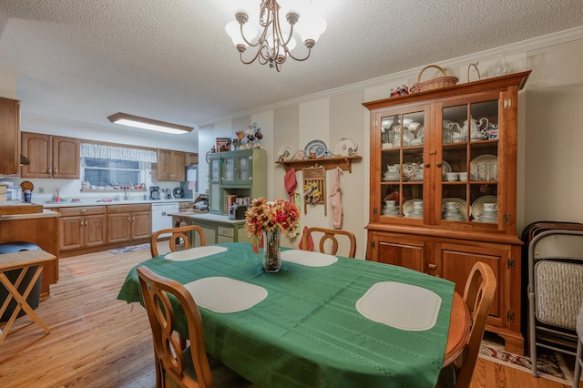 dining area with a notable chandelier, light hardwood / wood-style flooring, a textured ceiling, and ornamental molding