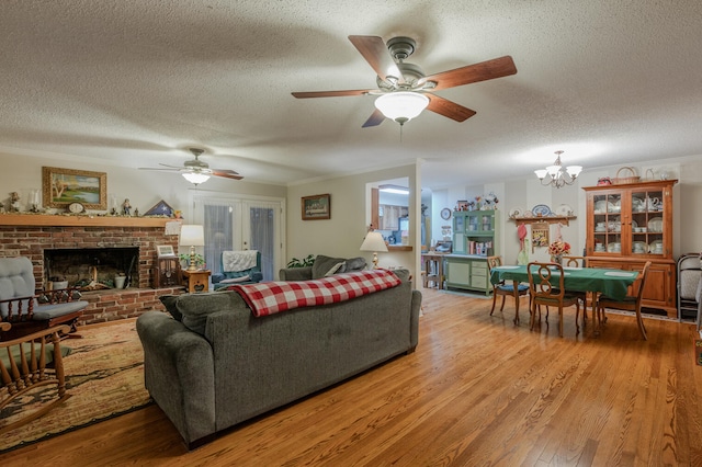 living room featuring a fireplace, a textured ceiling, light wood-type flooring, and ceiling fan with notable chandelier