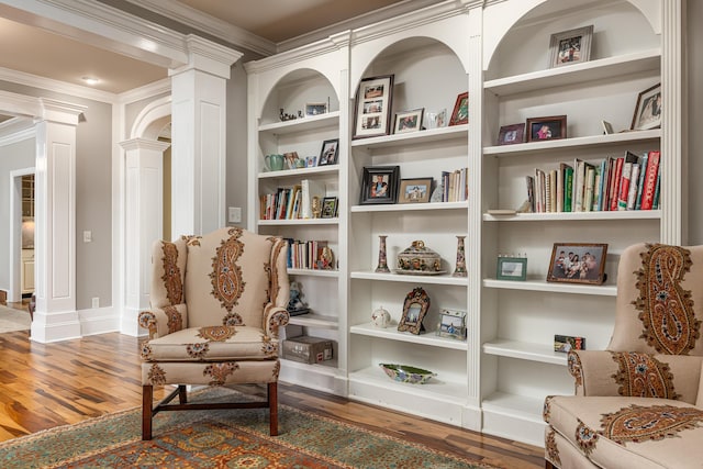 living area featuring hardwood / wood-style flooring, built in features, ornamental molding, and decorative columns