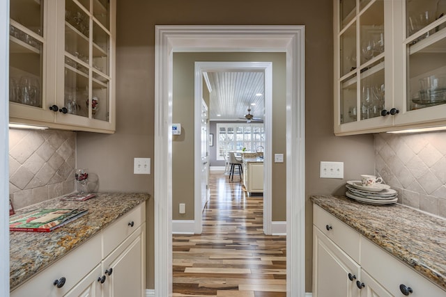 bar featuring decorative backsplash, white cabinetry, light hardwood / wood-style flooring, and light stone counters