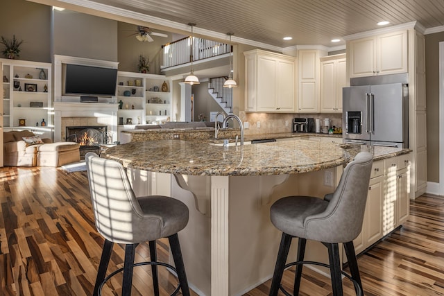 kitchen with high end refrigerator, hanging light fixtures, ceiling fan, light stone countertops, and a breakfast bar area