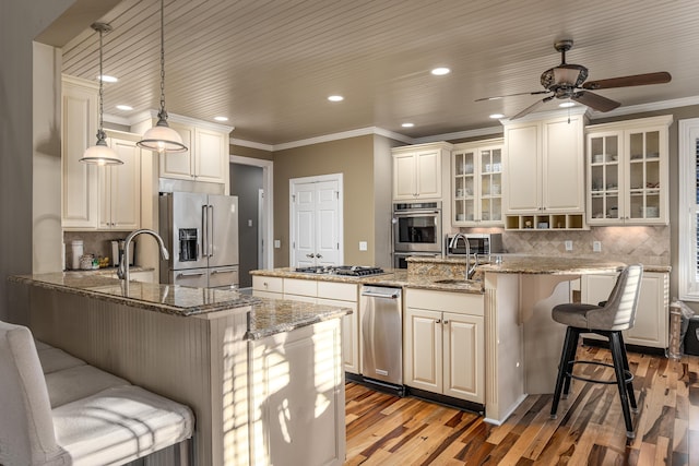 kitchen featuring appliances with stainless steel finishes, pendant lighting, light hardwood / wood-style flooring, stone counters, and a breakfast bar area