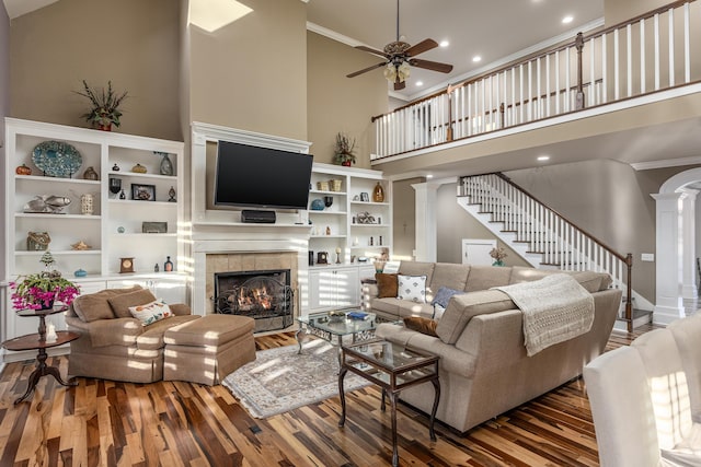 living room with a towering ceiling, ornamental molding, ceiling fan, wood-type flooring, and a fireplace