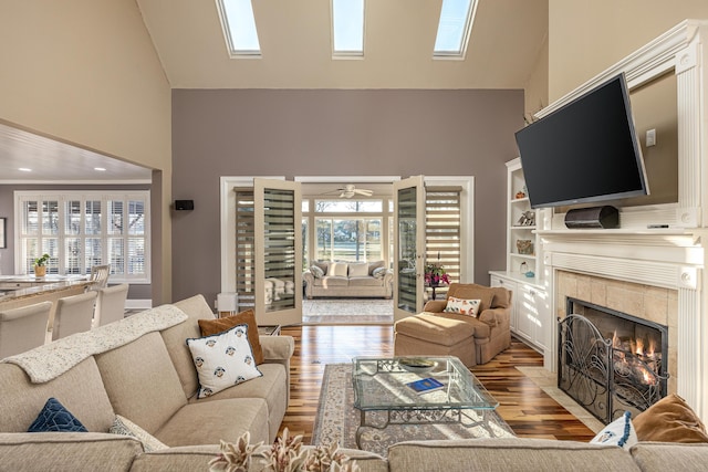 living room with ceiling fan, a tile fireplace, high vaulted ceiling, built in features, and light hardwood / wood-style floors