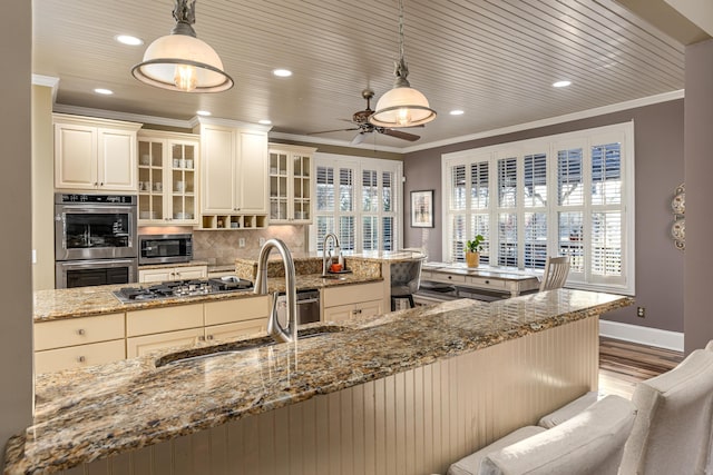 kitchen featuring light stone counters, light wood-type flooring, hanging light fixtures, and appliances with stainless steel finishes