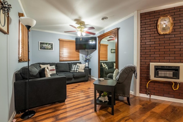 living room featuring ceiling fan, heating unit, wood-type flooring, a fireplace, and ornamental molding