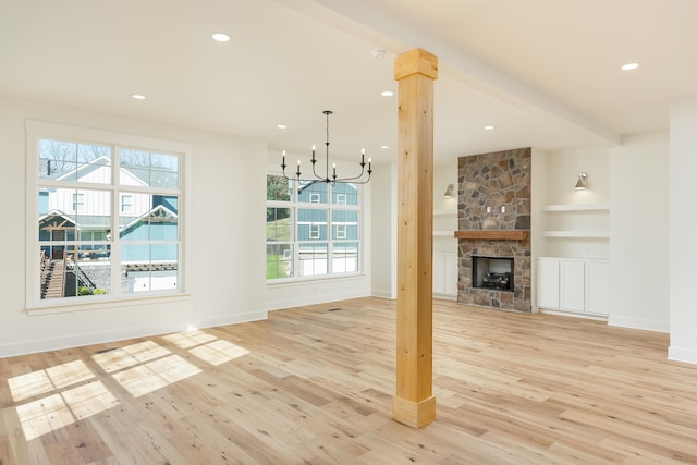 unfurnished living room featuring beam ceiling, a fireplace, light hardwood / wood-style floors, and an inviting chandelier