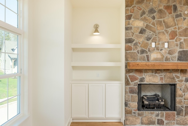 unfurnished living room with a stone fireplace, built in features, and light wood-type flooring