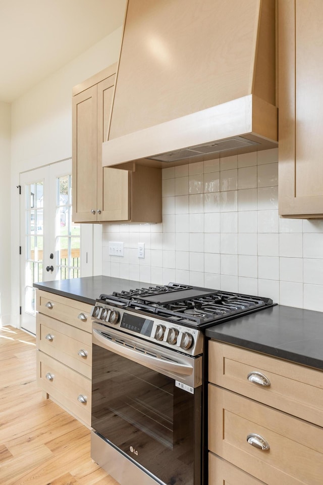 kitchen with gas stove, light brown cabinets, tasteful backsplash, custom exhaust hood, and light wood-type flooring