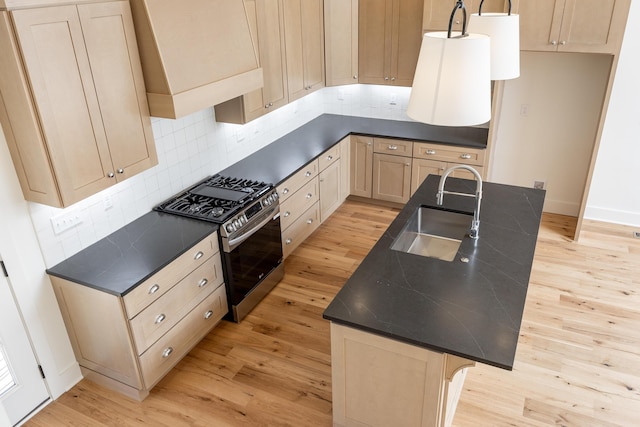 kitchen with stainless steel gas range oven, backsplash, sink, an island with sink, and light hardwood / wood-style floors