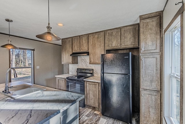 kitchen featuring light wood-type flooring, black appliances, a sink, decorative light fixtures, and under cabinet range hood