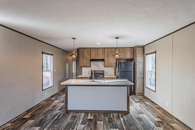 kitchen with dark wood finished floors, hanging light fixtures, freestanding refrigerator, and a wealth of natural light