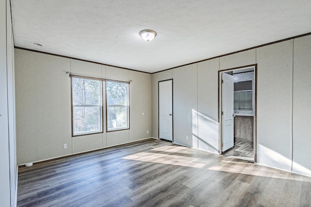 unfurnished bedroom featuring connected bathroom, a textured ceiling, wood finished floors, and crown molding