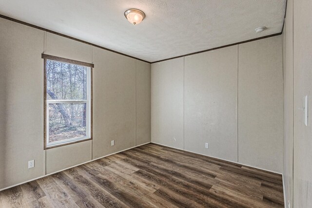 empty room with a textured ceiling, crown molding, and wood finished floors