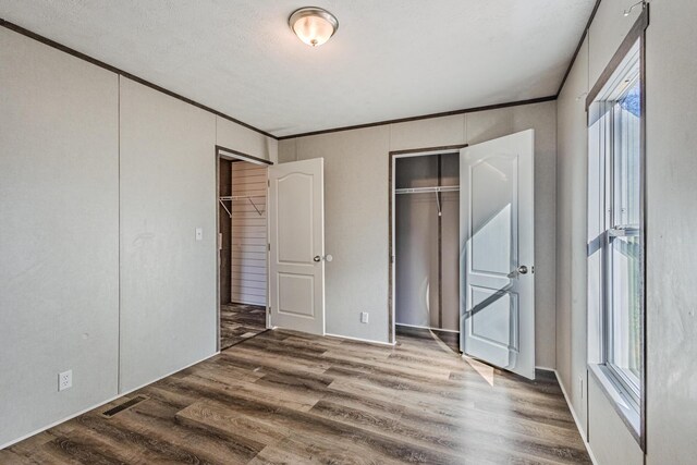 unfurnished bedroom featuring crown molding, wood finished floors, visible vents, and a closet