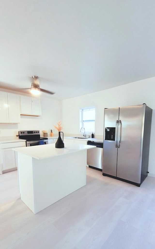 kitchen with sink, a kitchen island, light hardwood / wood-style floors, white cabinetry, and stainless steel appliances