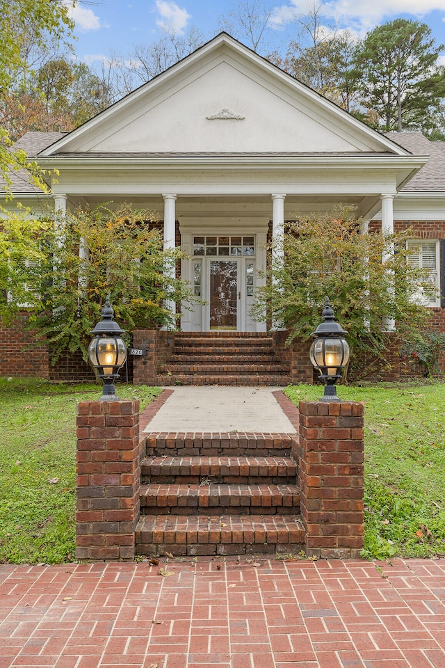 view of exterior entry with a porch and a lawn