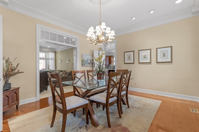 dining space with light hardwood / wood-style floors, an inviting chandelier, and ornamental molding