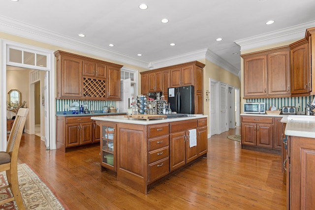 kitchen with wood-type flooring, tasteful backsplash, black fridge, and a kitchen island