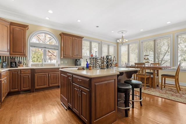 kitchen featuring hanging light fixtures, a chandelier, light wood-type flooring, a kitchen island, and ornamental molding