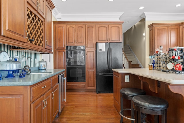 kitchen featuring a kitchen breakfast bar, light wood-type flooring, backsplash, ornamental molding, and black appliances