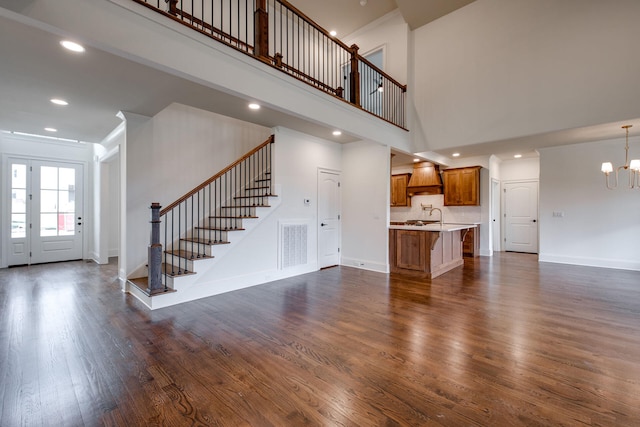 unfurnished living room featuring a chandelier, sink, dark wood-type flooring, and a high ceiling