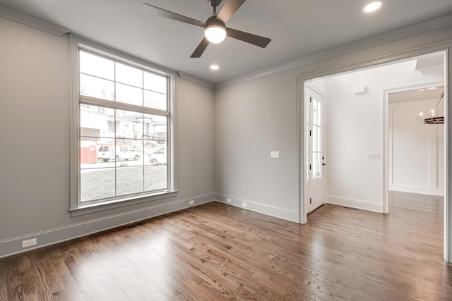 unfurnished room featuring wood-type flooring, ceiling fan with notable chandelier, a wealth of natural light, and ornamental molding