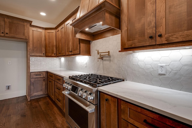 kitchen featuring light stone countertops, dark hardwood / wood-style flooring, premium range hood, decorative backsplash, and stainless steel stove