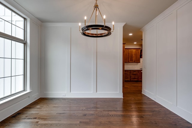 unfurnished dining area with dark wood-type flooring and a notable chandelier