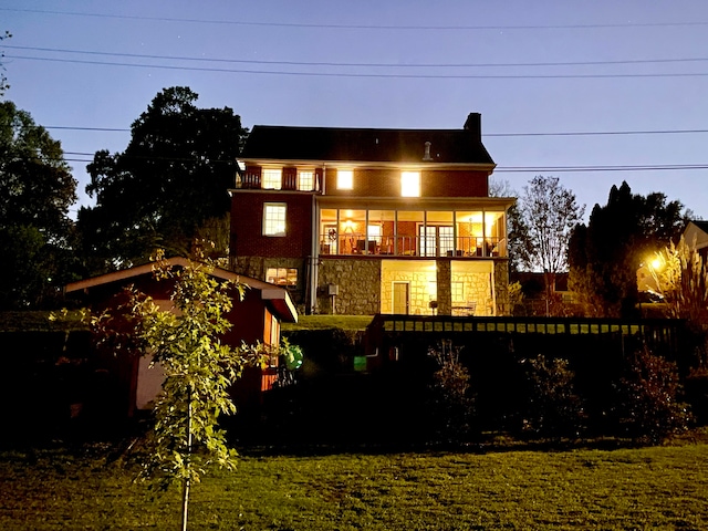 back house at dusk featuring a lawn and a balcony