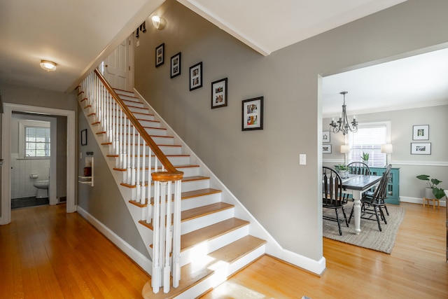 staircase featuring a notable chandelier, wood-type flooring, ornamental molding, and tile walls